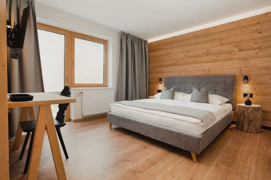 Apartment Auszeit Stoacherhof – Schlafzimmer mit Doppelbett vor Zirbenholzwand, Schreibtisch und Baumstamm-Nachttisch | Ferienwohnung Wipptal Tirol