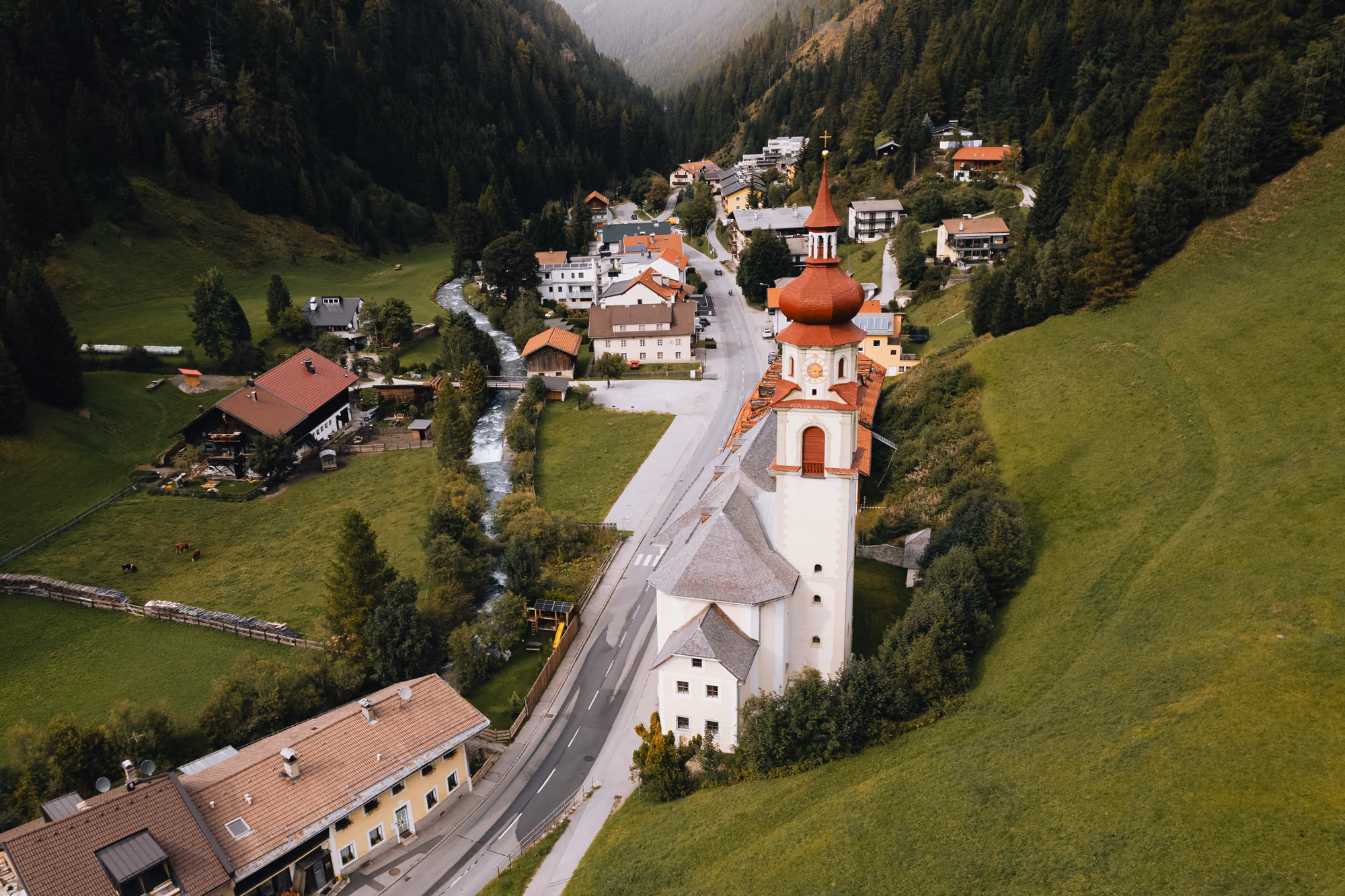 Blick von oben auf den Ortskern von Gries am Brenner mit der Kirche und ihrem roten Zwiebelturm im engen Tal