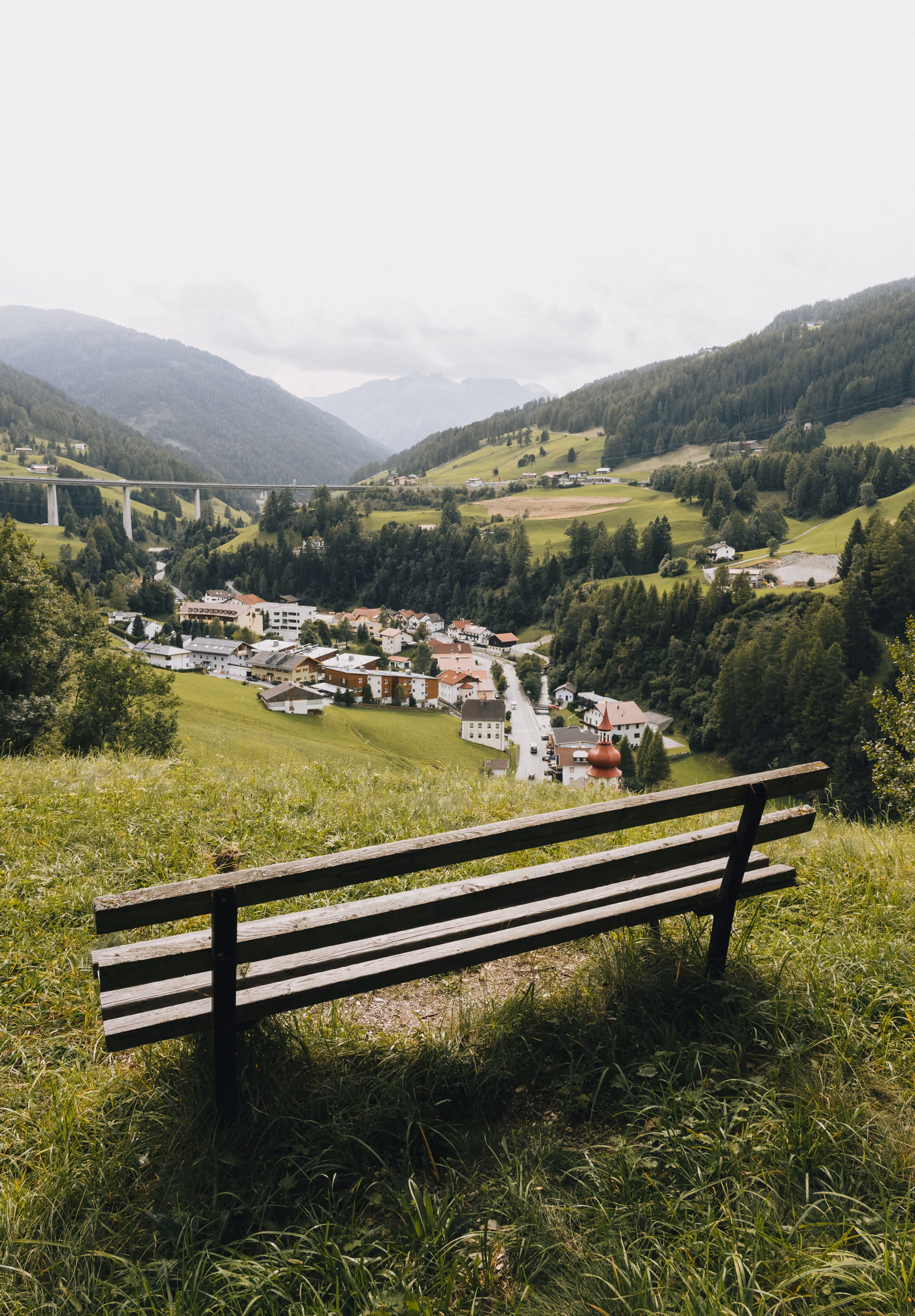 Holzbank auf einer Bergwiese mit Blick über Gries am Brenner und das Viadukt der Brennerautobahn