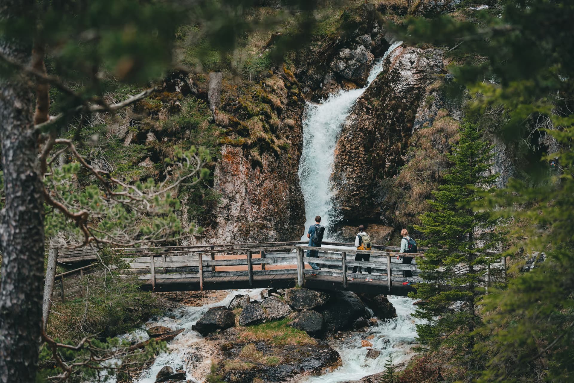 Wasserfall bei Trins im Gschnitztal – Wanderer auf einer Holzbrücke vor der Kaskade im Wald
