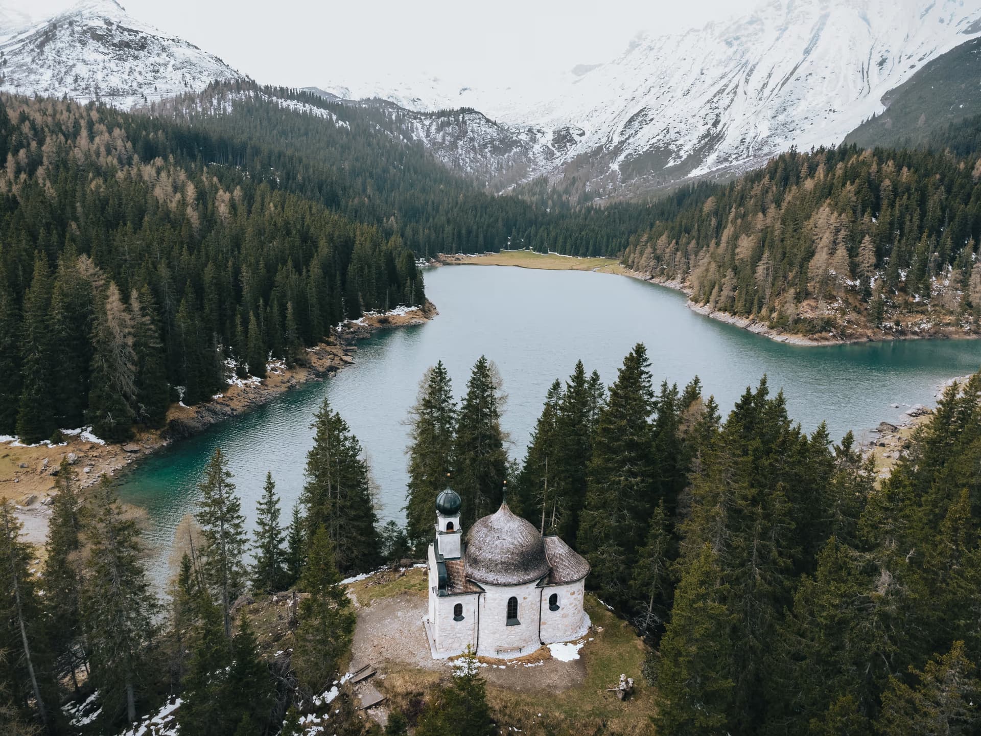 Obernberger See von oben mit der Seekapelle und verschneiten Gipfeln im Wipptal