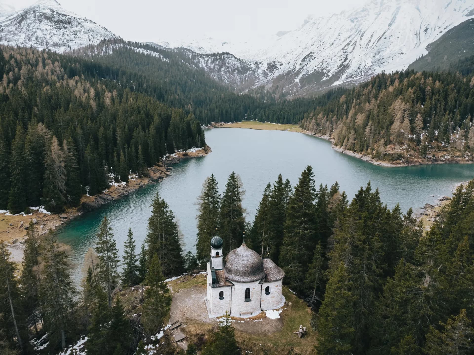 Obernberger See von oben mit der Seekapelle und verschneiten Gipfeln im Wipptal