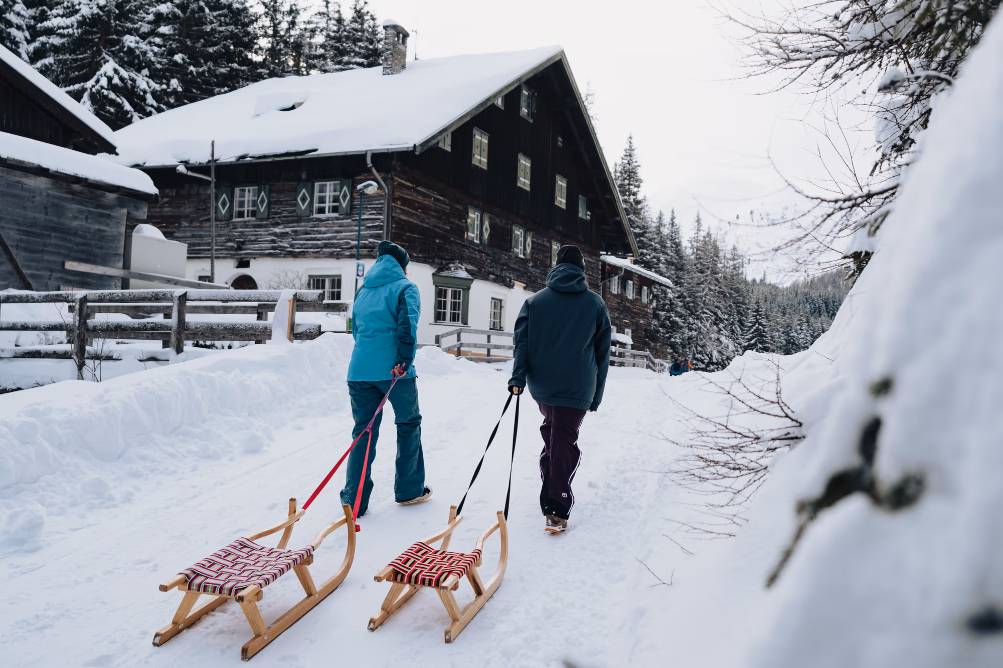 Rodeln im Obernbergtal – zwei Gäste ziehen Hörnerschlitten vor einem verschneiten Tiroler Bauernhaus