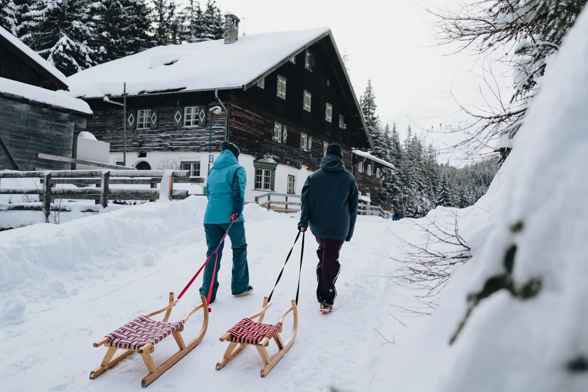 Rodeln im Obernbergtal – zwei Gäste ziehen Hörnerschlitten vor einem verschneiten Tiroler Bauernhaus
