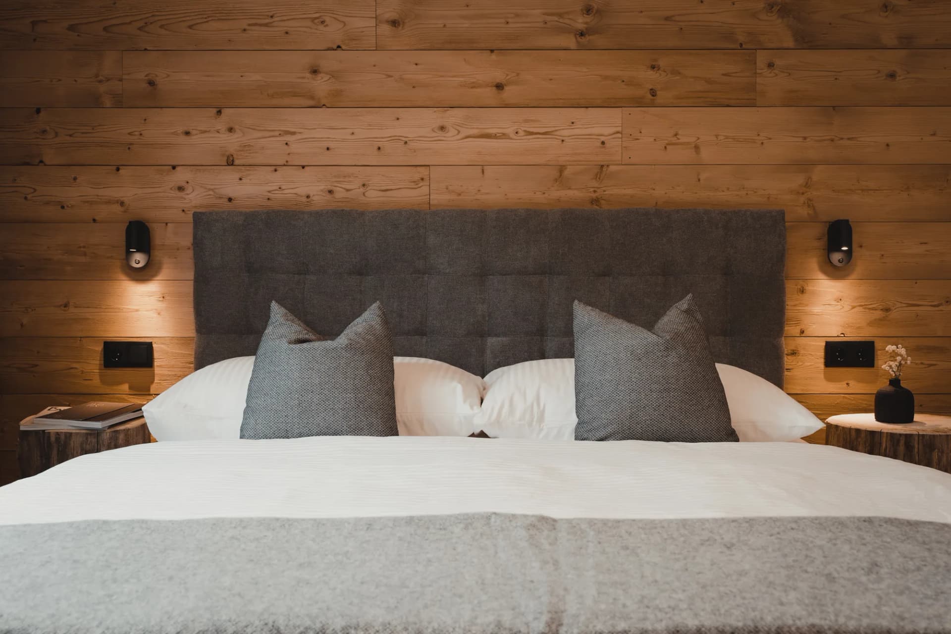 Auszeit apartment Stoacherhof – double bed with upholstered headboard, two reading lamps and tree-trunk bedside tables against a reclaimed wood wall | holiday flat Wipptal Tyrol