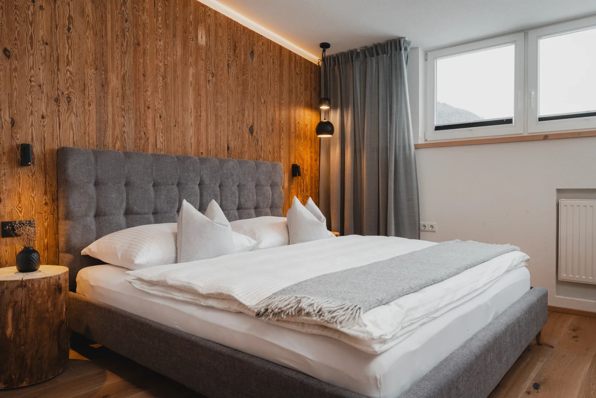 Panorama apartment Stoacherhof – bedroom with double bed against a reclaimed wood wall, pendant lamp and window front | holiday flat Wipptal Tyrol