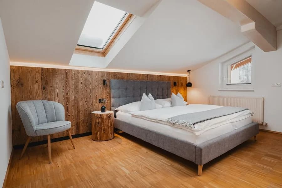 Panorama apartment Stoacherhof – bedroom under the sloping roof with skylight, double bed and upholstered armchair | holiday flat Wipptal Tyrol
